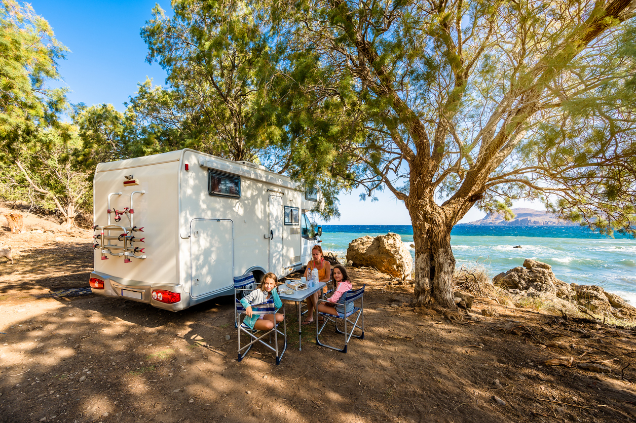 Famille voyageant en camping-car prenant le petit-déjeuner sur une plage de Grèce. © iStock / _jure